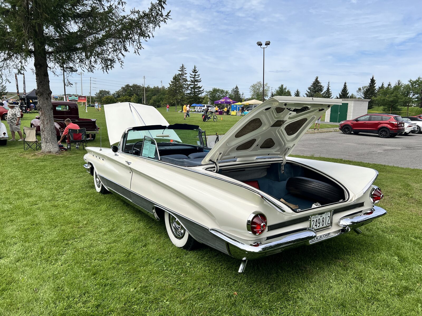 Rear three-quarter view of the white 1960 Buick convertible with its trunk lid raised, showing the tail fins and chrome bumper.
