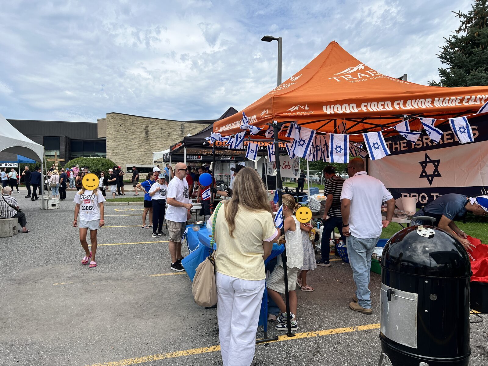 Visitors and cooking teams under canopies strung with Israeli flags at the Ottawa Kosher BBQ Cook-Off, a large smoker in the foreground.