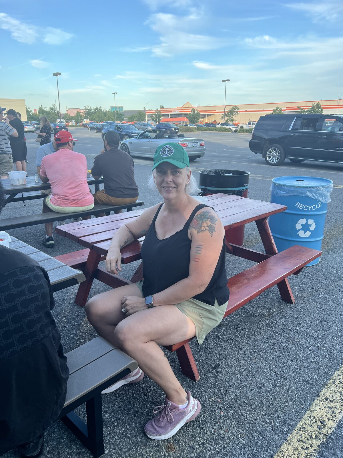 Shawna Thibodeau, who runs Shawna's Outreach, sitting at a red picnic table in the Fat Les's lot wearing a green Fat Les's Chip Stand cap.