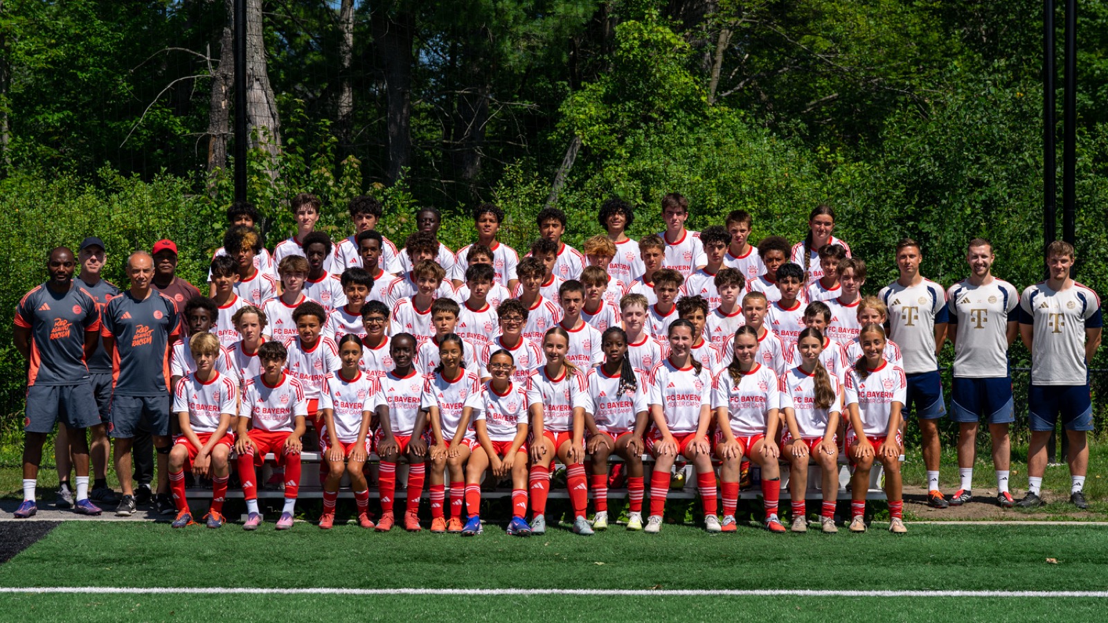 Participants and coaches from the FC Bayern soccer camp at Nepean Hotspurs, in matching red and white kit, posed together on a turf field.