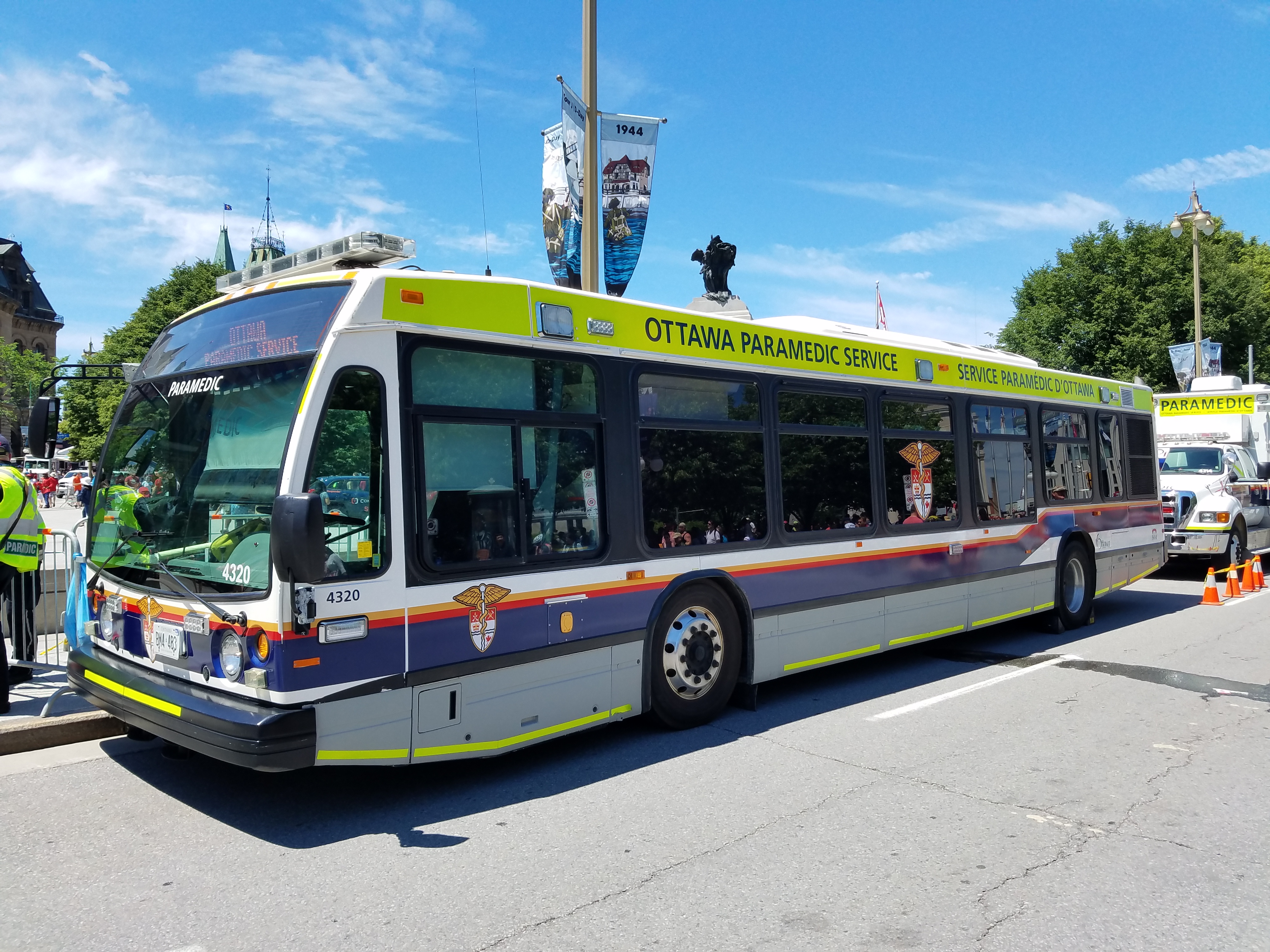 An Ottawa Paramedic Service bus (unit 4320) bearing the bilingual 'Ottawa Paramedic Service / Service paramédical d'Ottawa' livery parked on a downtown Ottawa street on a sunny day.