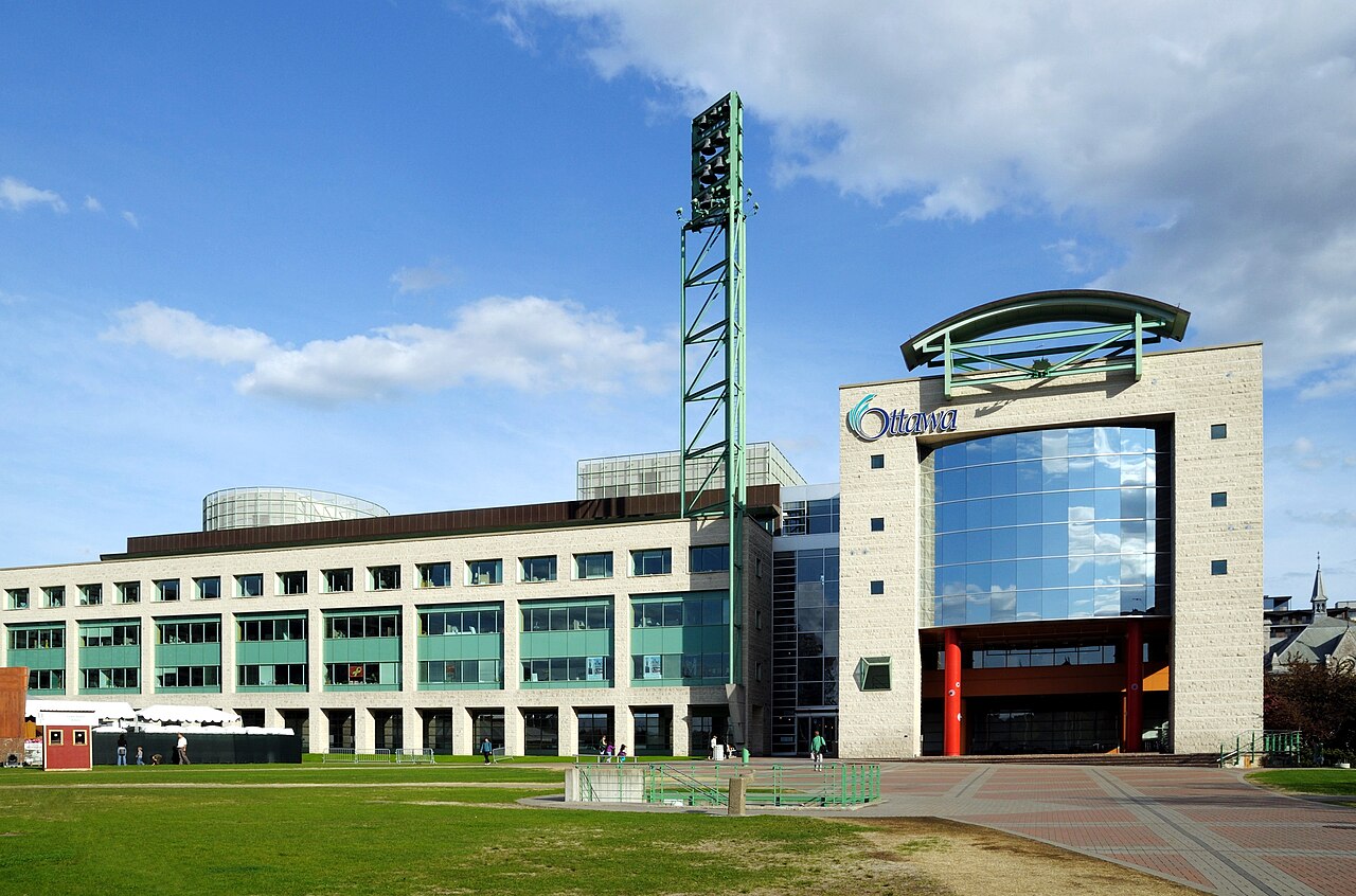 The front of Ottawa City Hall on Laurier Avenue, with its bell tower and Ottawa sign, on a sunny day.